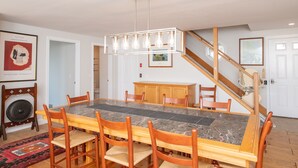 A dining area with a marble table, wooden chairs, a chandelier, a staircase, and a framed picture on the wall. - Family & Pet Getaway | Scenic Views |Cape Cod Home (Wellfleet)