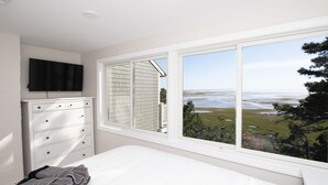A bedroom with a large window offering a view of the ocean and a grassy landscape. - Family & Pet Getaway | Scenic Views |Cape Cod Home (Wellfleet)