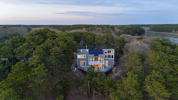 A modern two-story house surrounded by dense forest, with solar panels on the roof. - Family & Pet Getaway | Scenic Views |Cape Cod Home (Wellfleet)