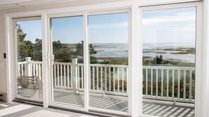 A large sliding glass door leading to a balcony with a view of a coastal landscape. - Family & Pet Getaway | Scenic Views |Cape Cod Home (Wellfleet)