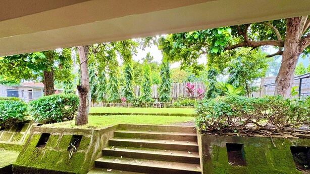 Escadaria de pedra que leva a um espaço coberto, com vista para um jardim bem cuidado e árvores.