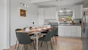 Una cocina moderna con armarios blancos, un refrigerador de acero inoxidable y un comedor con mesa dispuesta para seis comensales.