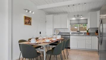 A modern kitchen with white cabinetry, a stainless steel refrigerator, and a dining area with a table set for six.