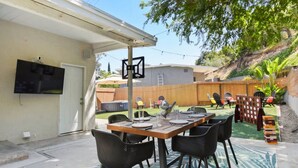 Un patio al aire libre con una mesa lista para comer, rodeada de sillas, y una zona de estar cubierta con sillas y una mesa.