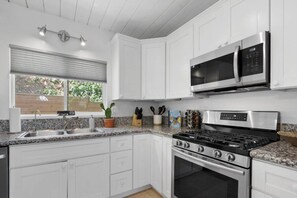 A modern kitchen with white cabinets, stainless steel appliances, a granite countertop, and a window with a view of greenery. - Sunnyside Resort Spa, Beach, Zoo, Arcade (La Mesa)