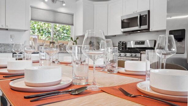 Una cocina moderna con armarios blancos, electrodomésticos de acero inoxidable y un comedor listo para una comida.