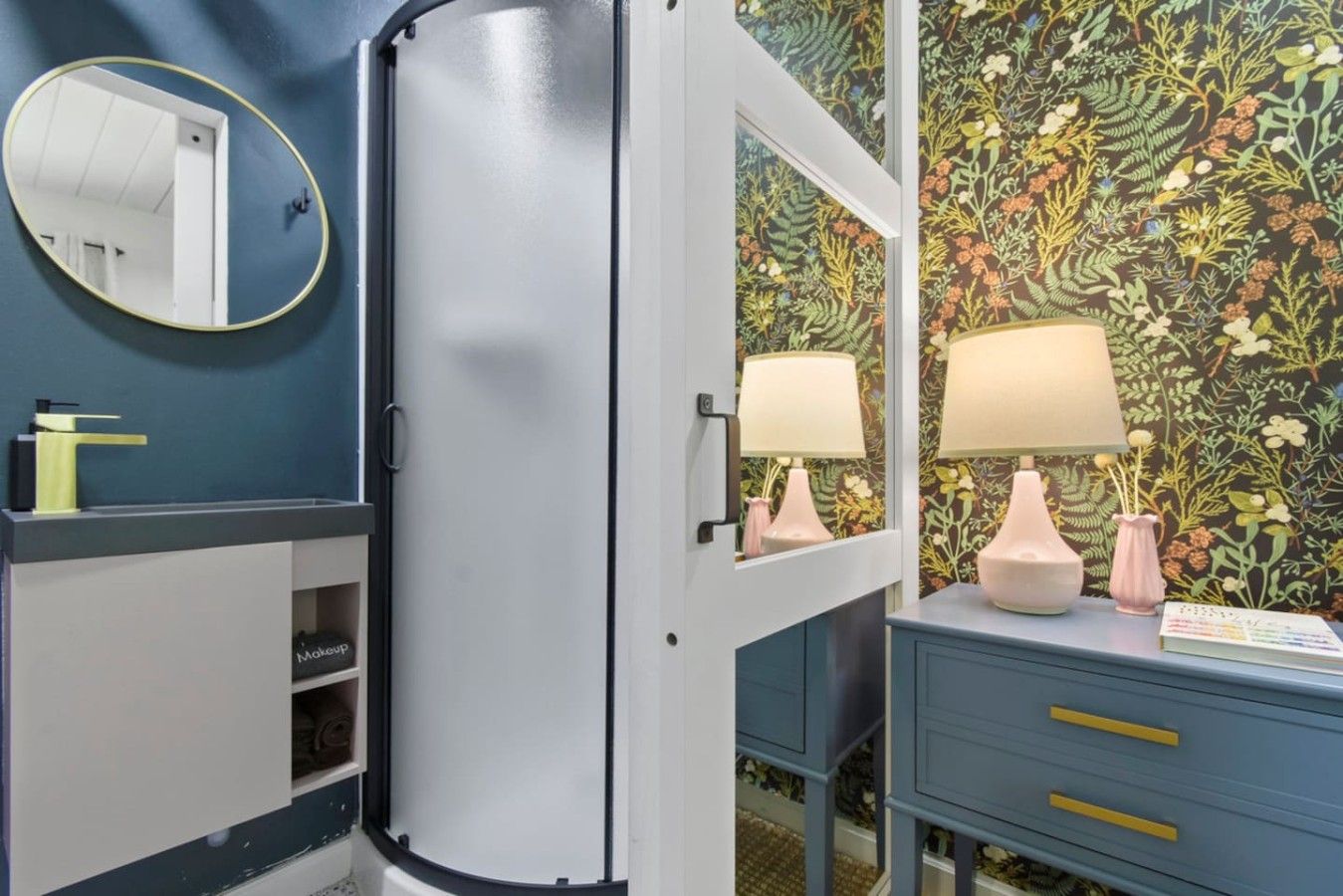 Un baño con espejo, lavamanos, armario y puerta con papel tapiz floral.