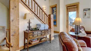 Una sala de estar acogedora con una escalera de madera, una chimenea, un sofá de cuero y un comedor con mesa y sillas.