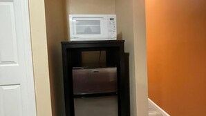 Une petite cuisine équipée avec un micro-ondes blanc et un petit réfrigérateur posé sur un meuble noir.