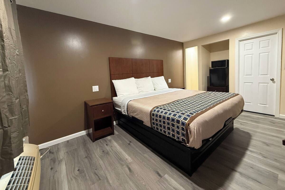 Een slaapkamer met een bed, nachtkastje, televisie en een deur.