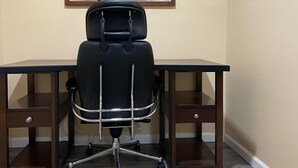 Une pièce avec un fauteuil de bureau noir, un bureau et un miroir au mur.