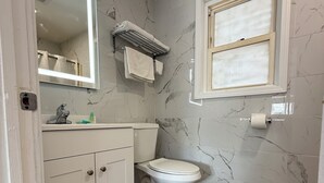 Une salle de bain avec un mur en marbre, des toilettes, un lavabo avec un miroir et une fenêtre.