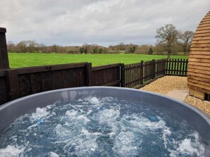 A hot tub in a backyard with a wooden fence and a grassy field in the background.