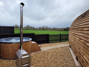 An outdoor hot tub area with a wooden deck and a view of a green field. - Rural Cosy Cabin with Wood-Fired Hot Tub (Whitchurch)