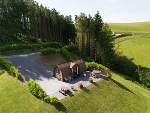 Eine kleine Hütte mit Kopfsteinpflasterweg, umgeben von Wald und Wiese.