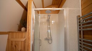 Ducha con puerta de vidrio, vigas de madera en el techo y un estante de metal.