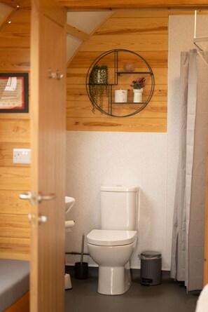Une petite salle de bain avec des toilettes blanches, une petite poubelle et un rideau de douche.