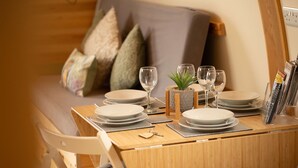 Una mesa de comedor de madera dispuesta con platos, vasos y cubiertos, con un cojín y almohadas en un sofá al fondo.