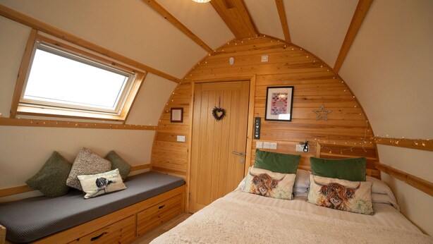 Una habitación acogedora con techo inclinado, un banco de madera con cojines, una cama con manta mullida y una ventana pequeña.
