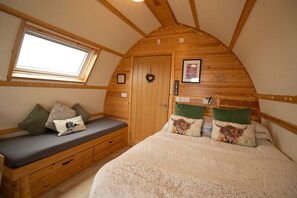 Una habitación acogedora con techo inclinado, un banco de madera con cojines, una cama con manta mullida y una ventana pequeña.