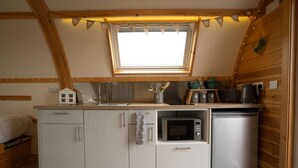Una cocina compacta con ventana, microondas, refrigerador pequeño y lavamanos.