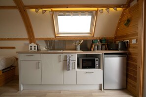 Una cocina compacta con ventana, microondas, refrigerador pequeño y lavamanos.