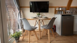 Una cocina moderna con televisor de pantalla plana, mesa de comedor de madera, sillas grises y refrigerador empotrado.