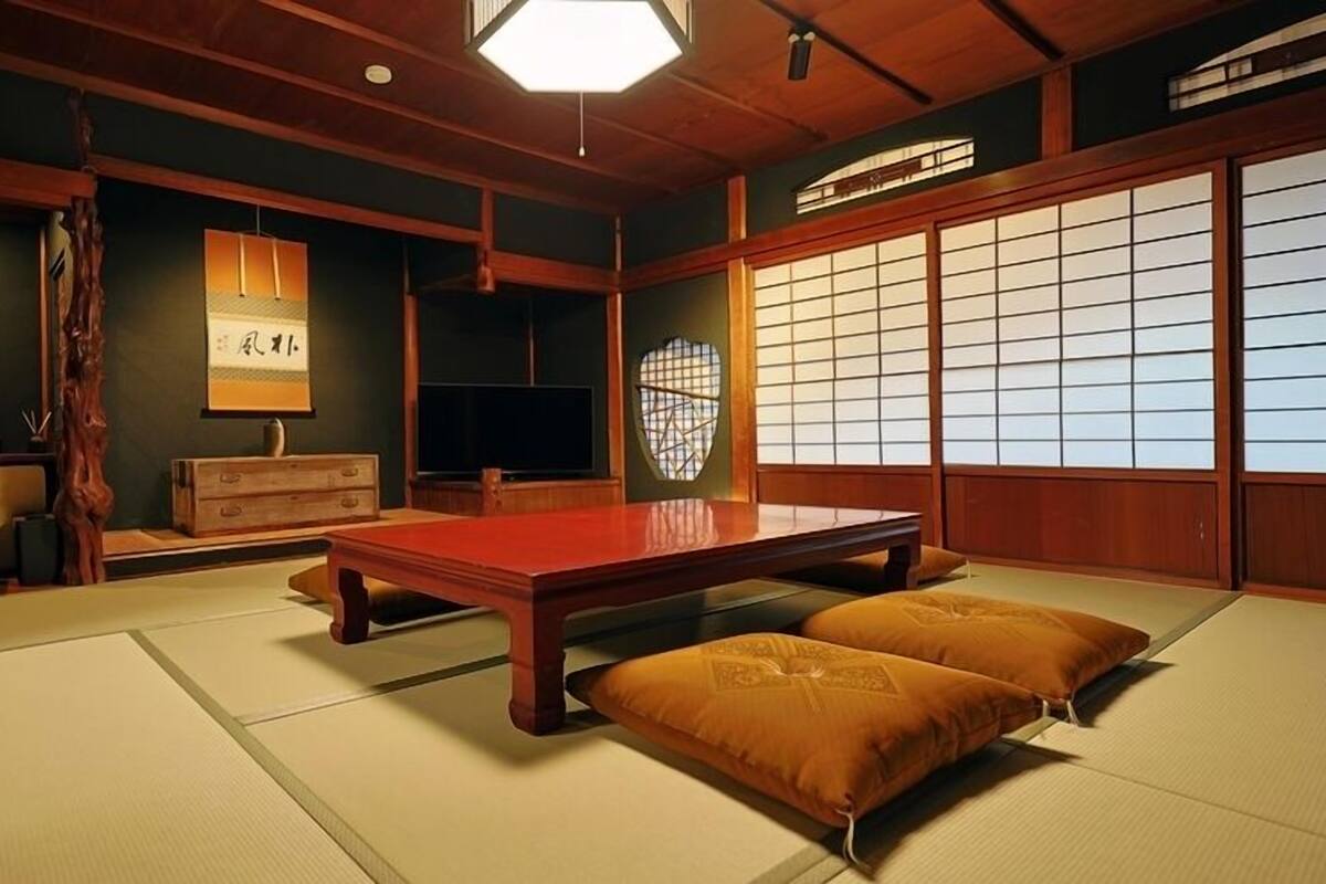 A traditional Japanese room with tatami flooring, a low wooden table, cushions, a shoji screen, and a hanging lantern.