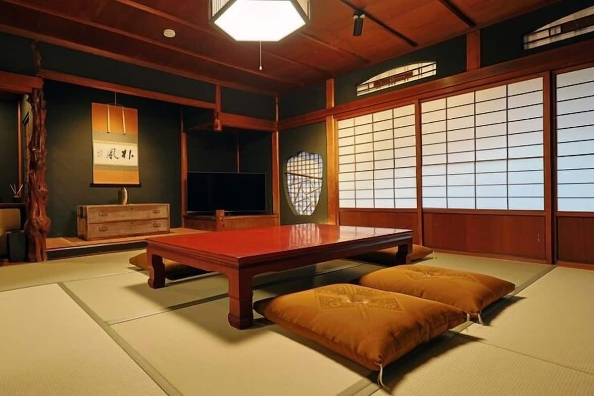 Una habitación tradicional japonesa con suelo de tatami, una mesa de madera baja, cojines, un divisor shoji y un farol colgante.