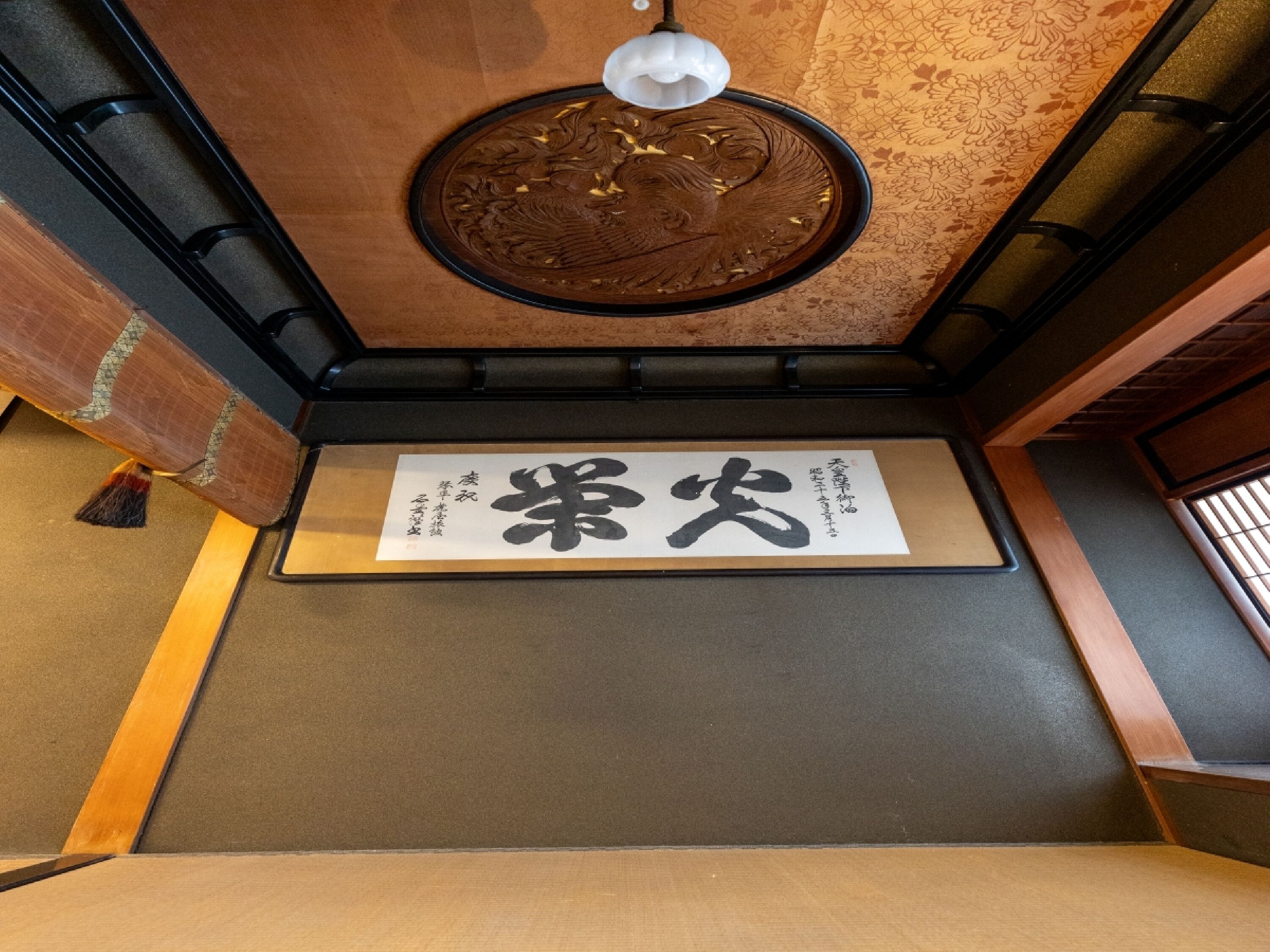 A traditional Japanese interior with tatami flooring, a shoji screen, and a hanging shoji with calligraphy.