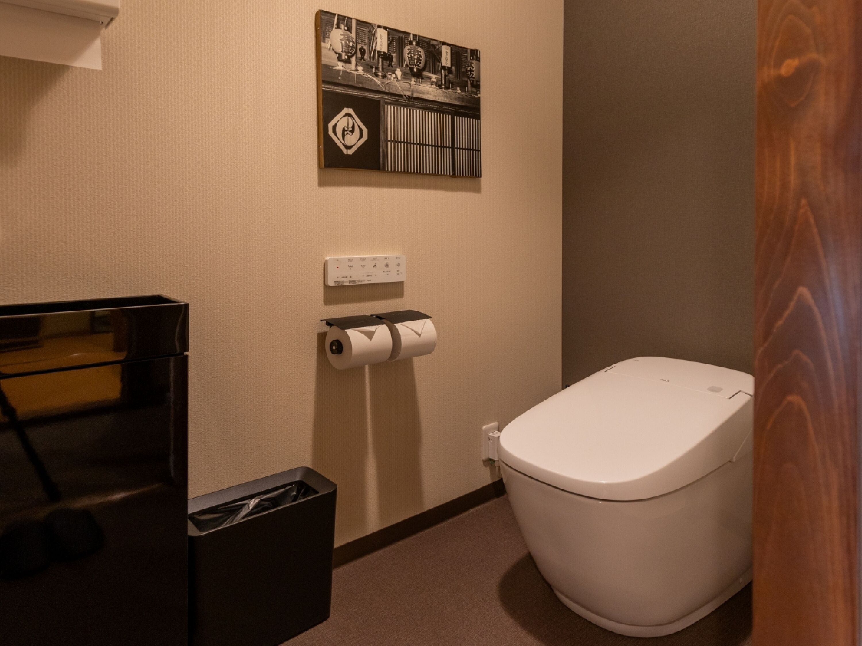 Een kleine, schone badkamer met toilet, een prullenbak en een toiletpapierhouder.