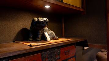 Un mueble de madera con una estatua de león encima, un cajón rojo con tiradores ornamentales y un jarrón pequeño en el suelo.