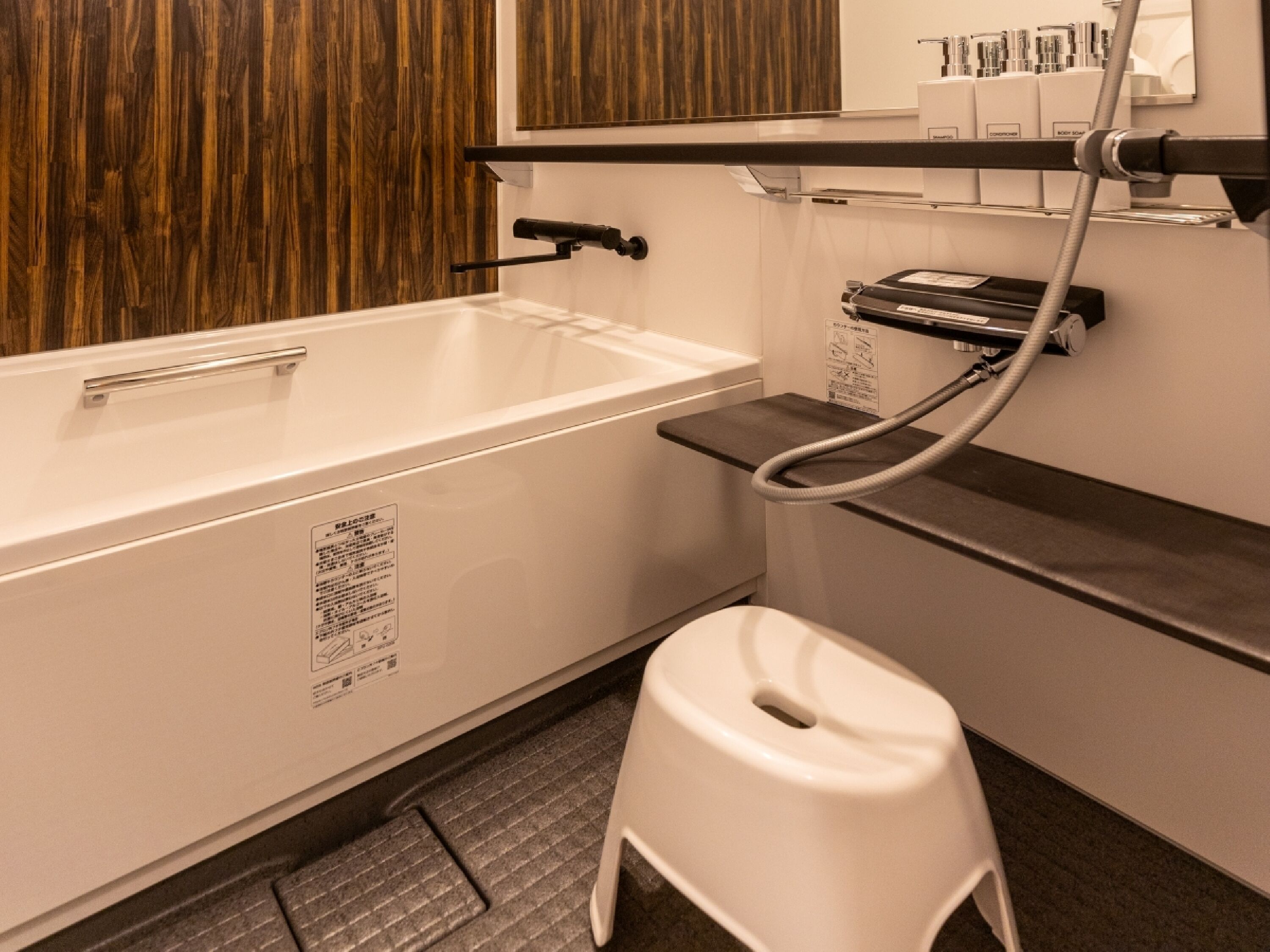 Une salle de bain avec une baignoire blanche, un petit tabouret blanc et un espace douche équipé d’un flexible.