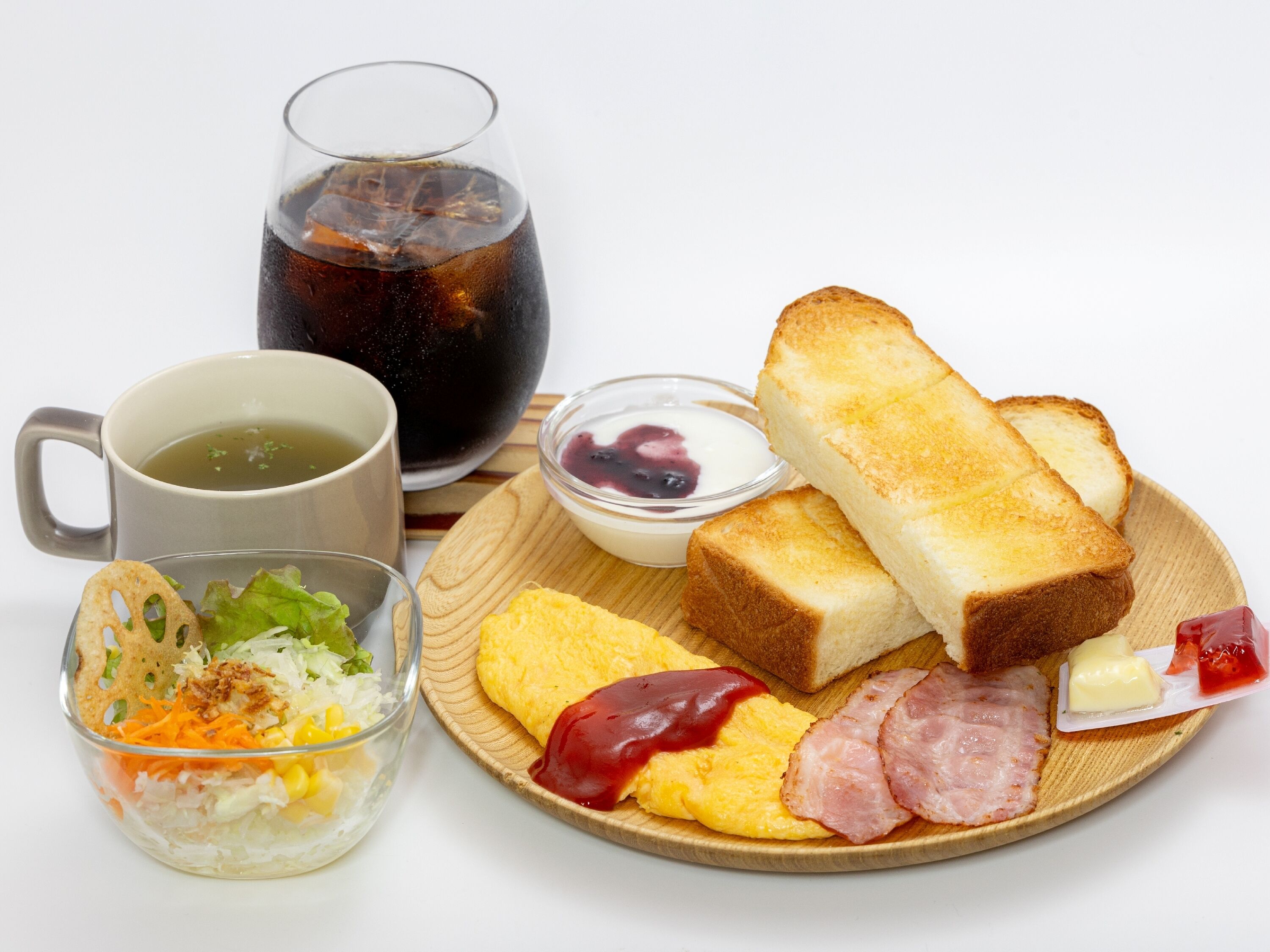 A breakfast plate with toast, eggs, ham, butter, ketchup, a glass of tea, a bowl of salad, and a cup of coffee.