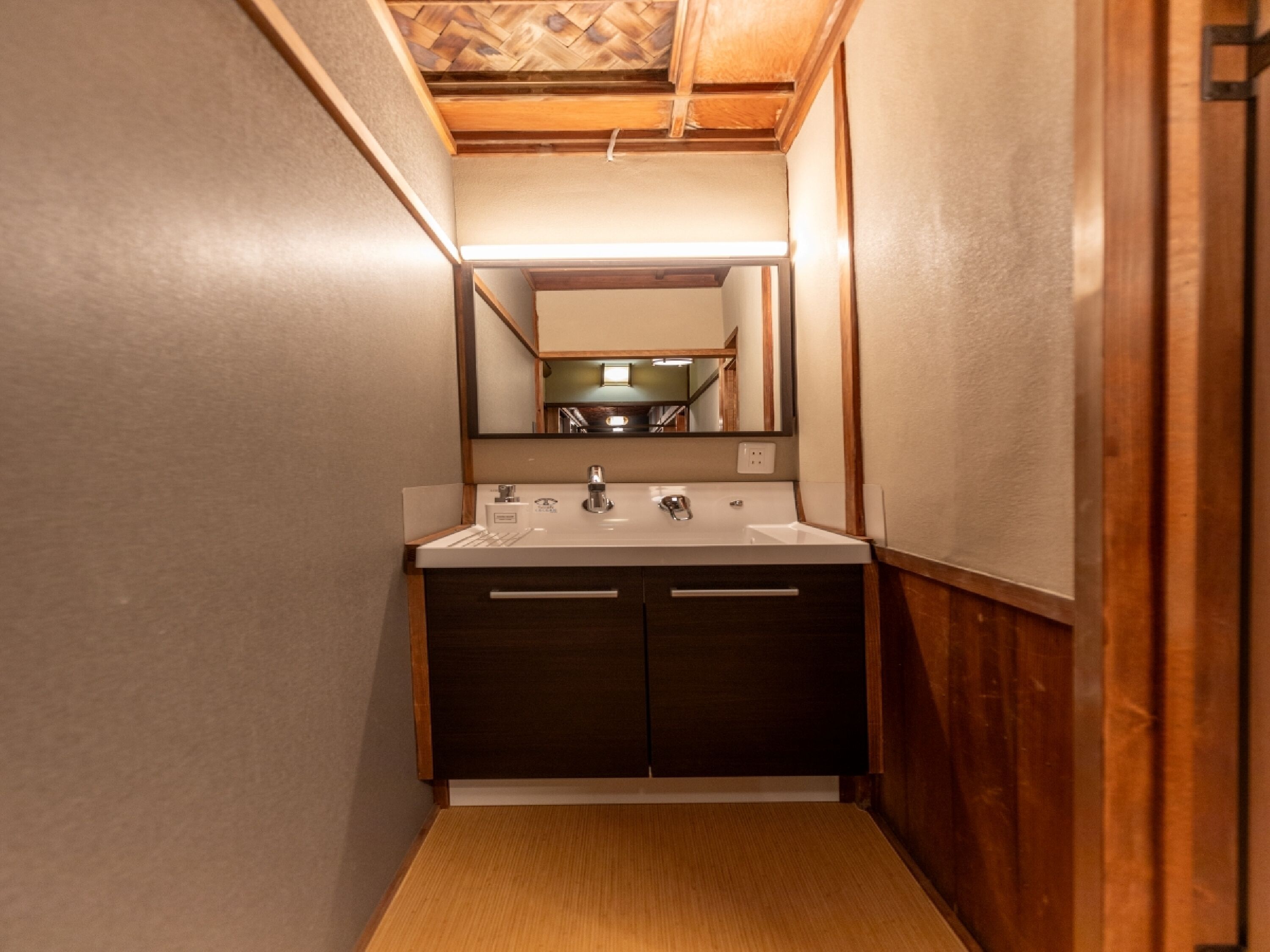 A narrow bathroom with a wooden vanity, a mirror, and a sink.