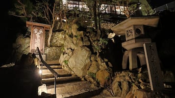 Un temple japonais traditionnel, avec des marches de pierre menant à une structure en bois, entouré de rochers et d’arbres.