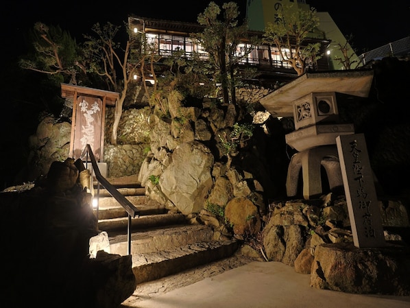 A traditional Japanese temple with stone steps leading up to a wooden structure, surrounded by rocks and trees. - Toraya Bekkan (Kotohira)