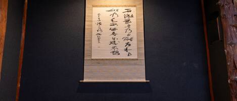 A traditional Japanese scroll with calligraphy, displayed in a wooden frame against a dark wall.