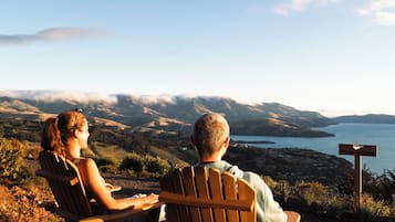 Two people sitting on wooden chairs facing a scenic view of a lake and mountains.