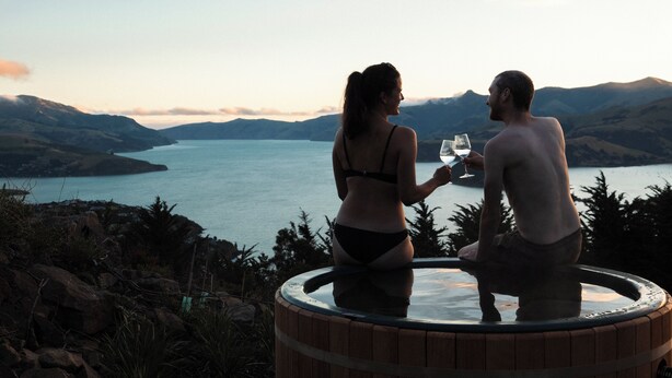 Twee personen zitten in een jacuzzi met uitzicht op een meer, met bergen op de achtergrond.