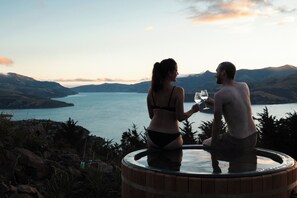Two people sitting on a hot tub overlooking a lake with mountains in the background. - Kūkupa Matairangi at Akaroa Lavender (Duvauchelle)