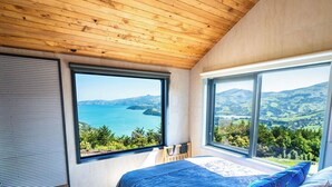 Een slaapkamer met een groot bed, twee ramen en uitzicht op een kustlandschap.