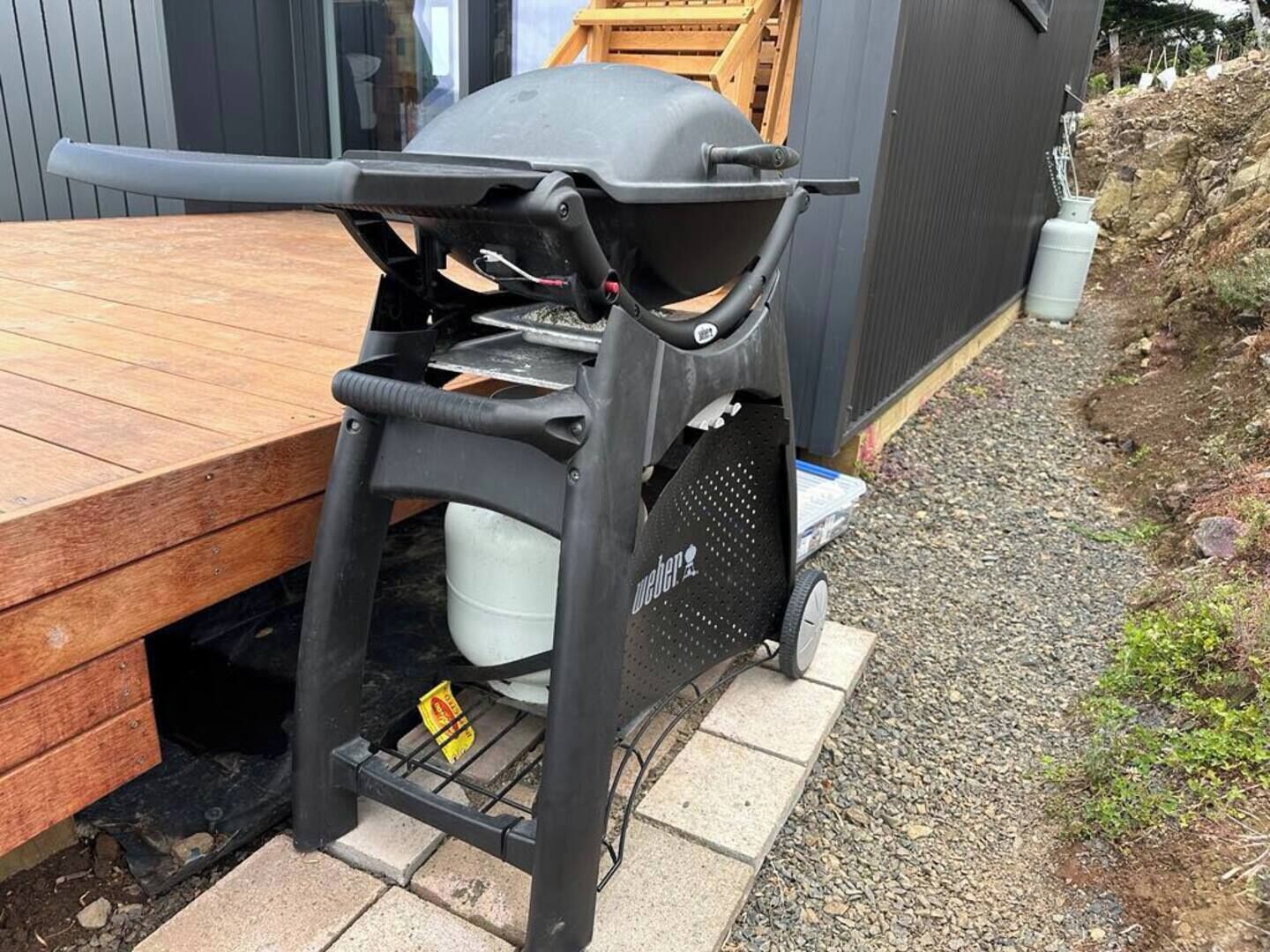 En portabel grill med metallram och hjul, placerad på ett trädäck.