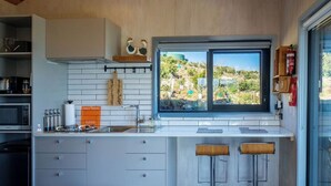 Een moderne keuken met een groot raam, witte kasten en twee barkrukken.