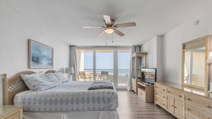 A bedroom with a bed, a television, a ceiling fan, and a view of the outdoors. - Ravishing Panoramic Vista | Inlet #608 (New Smyrna Beach)