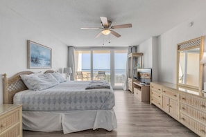 A bedroom with a bed, a television, a ceiling fan, and a view of the outdoors.