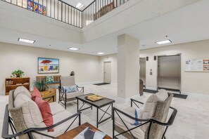 A lobby with a high ceiling, a staircase, a reception desk, and a seating area with chairs and a sofa.