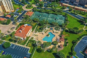 Luchtbeeld van een hotel met een zwembad, tennisbanen en een parkeerplaats.