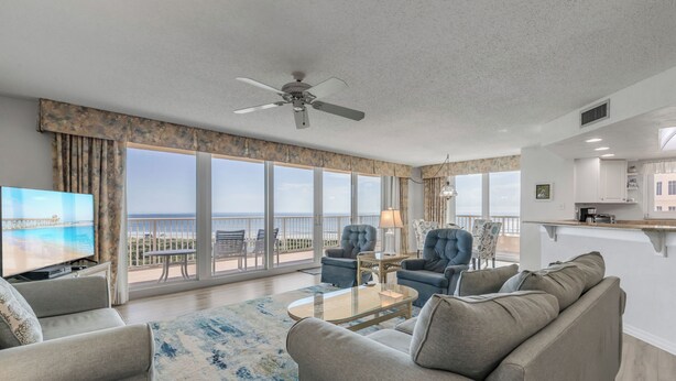 A spacious living room with a large TV, comfortable seating, a ceiling fan, and a view of the ocean. - Ravishing Panoramic Vista | Inlet #608 (New Smyrna Beach)