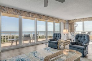 A spacious room with a large balcony overlooking the beach, featuring two armchairs, a coffee table, and a lamp. - Ravishing Panoramic Vista | Inlet #608 (New Smyrna Beach)